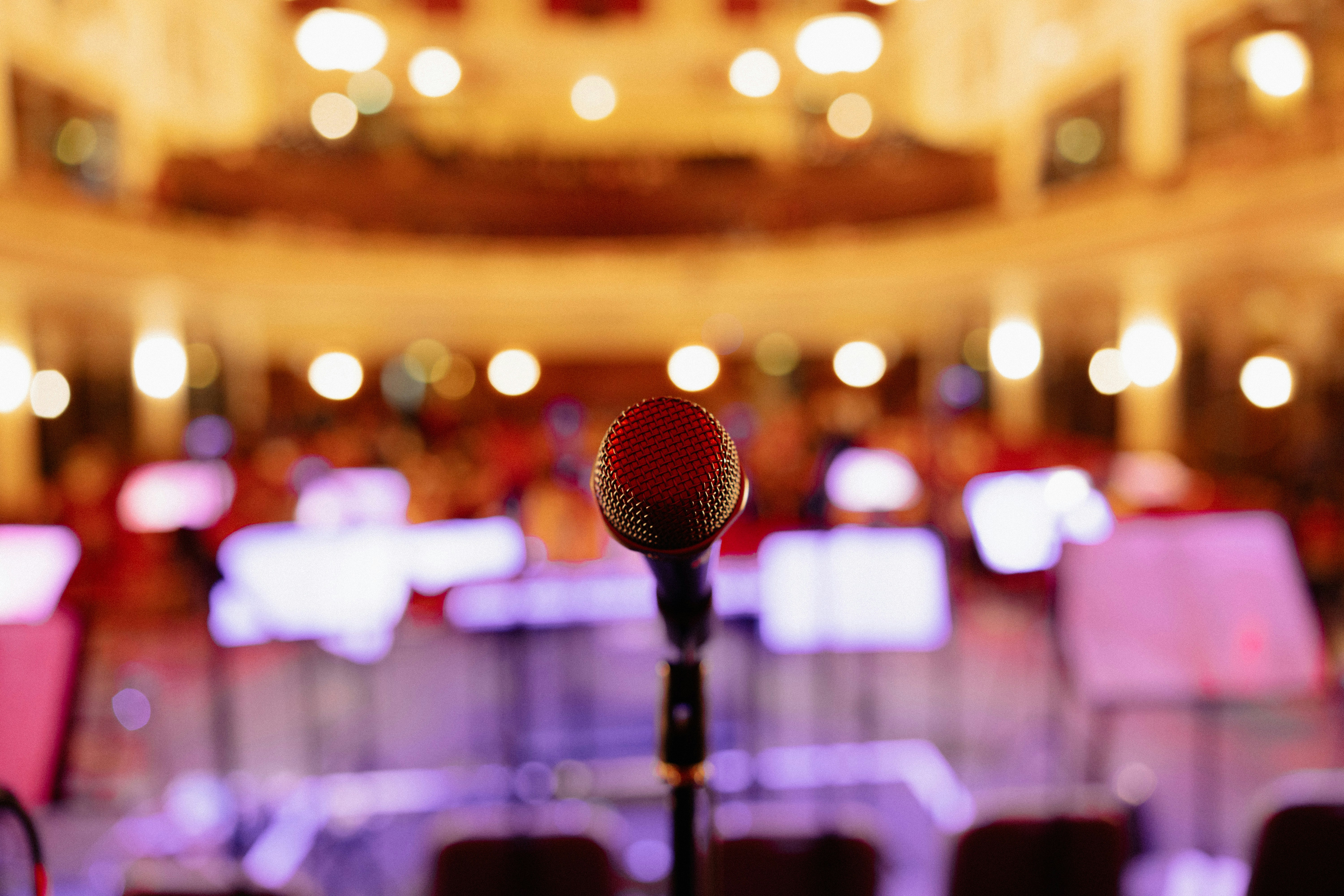 A microphone on a stage with warm lights and an audience space in the background